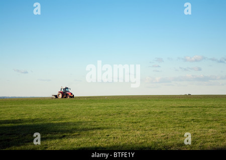 Ein Traktor auf dem Horizont schneiden Rasen in einem Feld, Newmarket, Suffolk, UK Stockfoto