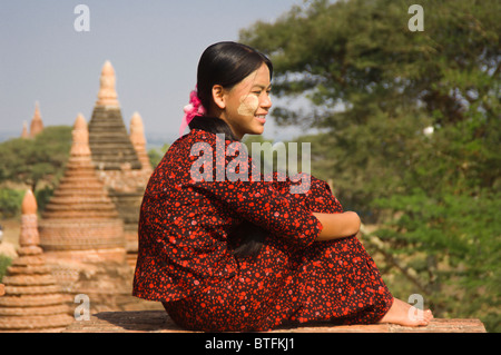 Junge burmesische Frau in einem roten Kleid sitzt auf dem Dach eines Tempels, Bagan (Pagan), Myanmar (Burma) Stockfoto