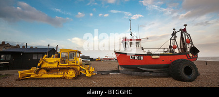 Gelbe Raupe Traktor mit einem roten Fischerboot auf einem Anhänger, am Strand von Aldeburgh geparkt Stockfoto