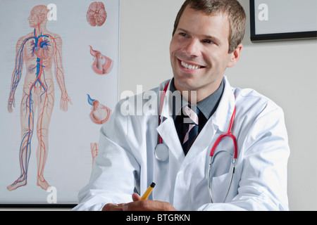 Arzt in seinem Büro mit Herz-Kreislauf-System Diagramm an Wand Stockfoto
