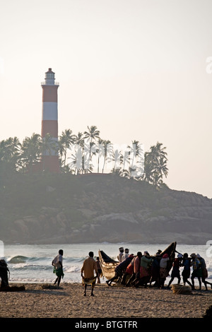 Einheimische Fischer, die Vorbereitung auf eine Fishingboat in das Meer am Strand von Kovalam in Kerala, Indien zu schieben Stockfoto