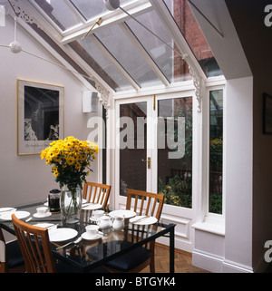 Vase mit gelben Blüten auf Glasplatte Tisch im modernen Wintergarten mit Glasdach und Flügeltüren Stockfoto