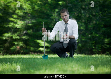 Geschäftsmann auf Rasen mit Schaufel und Glas mit Münzen Stockfoto