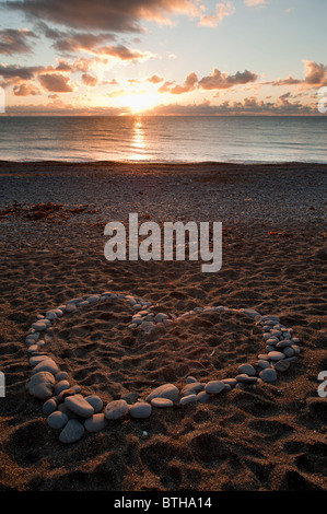 Eine Herzform gemacht Stein Steine Felsen Kiesel bei Sonnenuntergang am Strand-Wales Aberystwyth UK Stockfoto