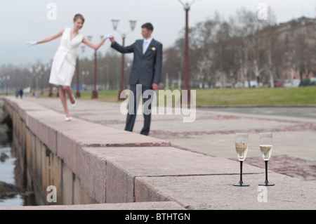 Just married jung schön Paar zu Fuß entlang des Kais von Petrosawodsk, Russland, mit Gläser Champagner. Gläser im Fokus Stockfoto