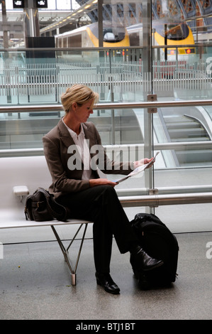 Porträt einer Geschäftsfrau Schneidersitz sitzen auf einem Sitz ein Papier in einem Bahnhof lesen Stockfoto