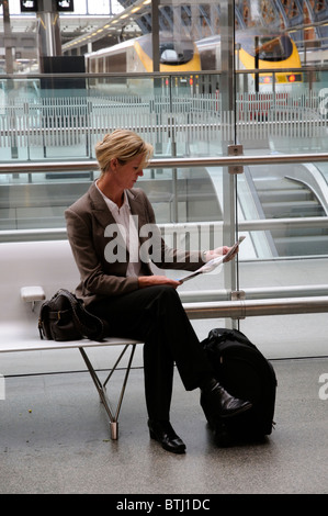 Porträt einer Geschäftsfrau Schneidersitz sitzen auf einem Sitz ein Papier in einem Bahnhof lesen Stockfoto