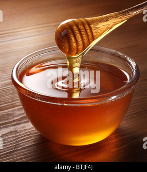 Honig aus Drizzler in die Schüssel gießen. Schüssel ist auf einem Holztisch. Stockfoto