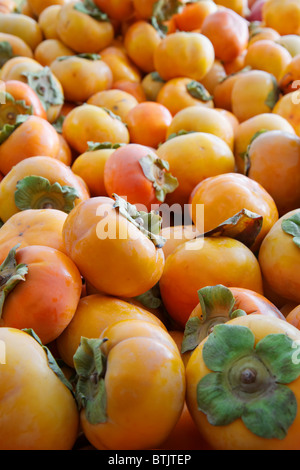 Haufen von Orange grün gekrönt Kaki auf dem Bauernmarkt Stockfoto