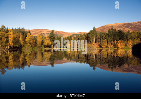 Glencoe man, Glen Coe, Argyll, Schottland. Herbstfärbung in Schottland vor dem Wintereinbruch. Herbstliche Bäume spiegeln perfekt Stockfoto