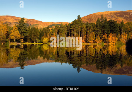 Glencoe man, Glen Coe, Argyll, Schottland. Herbstfärbung in Schottland vor dem Wintereinbruch. Herbstliche Bäume spiegeln perfekt Stockfoto