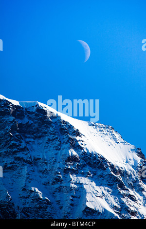 Ein Viertel Mond aufgeht über die Alpen Stockfoto