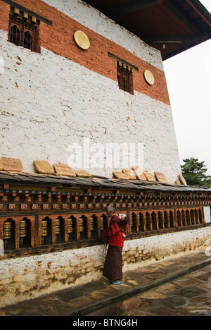 Eine Bhutan alte Frau mit einem Baby drehen die Gebetsmühlen außerhalb der wichtigsten Gebäude von Changangkha Lhakhang in Thimphu Stockfoto