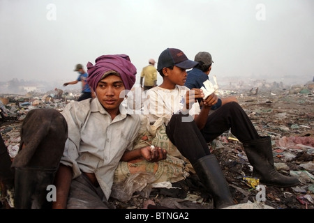 Zwei junge Männer sitzen in einem Haufen Müll auf einer verschmutzten Mülldeponie in Kambodscha. Stockfoto