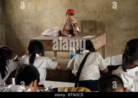 Ein 4 Jahre Alter asiatischen Jungen sitzt auf einem Lehrerpult an The Ban Buamlao Primary School in Ban Buamlao, Laos. Stockfoto