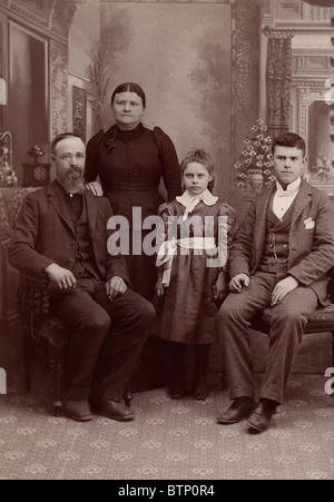 1890 vintage Foto Familie in einer formalen Studio erschossen. Dieses Foto ist vergilbt mit Alter. Sitzen ist Vater und Sohn mit Mutter und Tochter stehen Stockfoto
