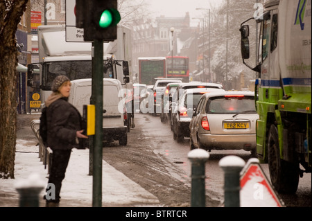 Starker Verkehr mit Schnee auf dem Boden. Anscheinend schwangere Frau durch Drücken der Taste an der Fußgängerampel. Stockfoto