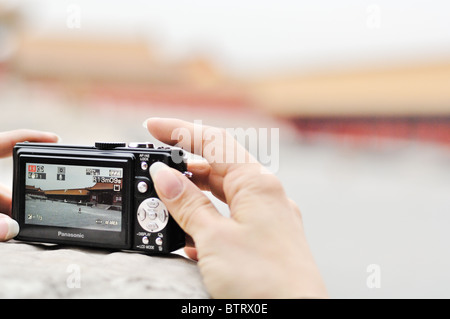 Junge Frau Hände halten eine kompakte Kamera in der verbotenen Stadt in Peking. Die Kamera wird an einer Wand aufgestellt. Der Hintergrund jedoch unscharf. Stockfoto