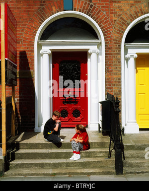 Kinder sitzen vor der georgischen Türen, Fitzwilliam Square, Dublin, Co. Dublin, Irland Stockfoto