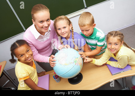 Porträt von Schülern und Lehrer Blick in die Kamera mit Globus auf Tisch im Erdkundeunterricht Stockfoto