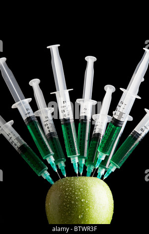 Spritzen stecken im Apple vor einem schwarzen Hintergrund Stockfoto