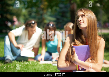 Porträt von Teenager-Mädchen mit Buch in Händen auf Grund ihrer Freunde lesen Stockfoto