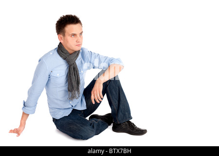 Lässige junger Mann in t-Shirt und Jeans sitzen auf dem Boden isoliert auf weißem Hintergrund, Exemplar auf der rechten Seite. Stockfoto
