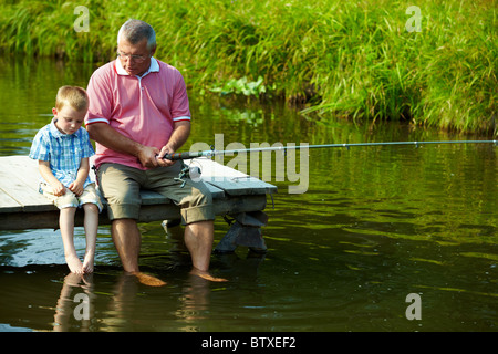 Foto von Großvater und Enkel auf Ponton mit den Füßen im Wasser sitzen und Angeln am Wochenende Stockfoto