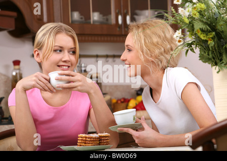 Zwei lächelnde Mädchen haben Tee und leckere Kekse in der Küche Stockfoto