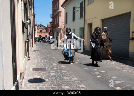 Schwarzen äthiopische afrikanischen Stammesangehörigen in traditionellen Kostümen tanzen auf der Straße um Geld für Essen, in einer kleinen italienischen Stadt betteln Stockfoto