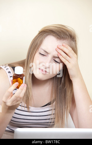 Ein junges Mädchen mit Kopfschmerzen prüft Hinweise auf eine Flasche Tabletten in ihr Schlafzimmer-UK Stockfoto