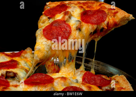 Stück Salami Pizza ganze Pizza mit Tomaten im Hintergrund entfernt. Auf schwarzem Hintergrund isoliert. Stockfoto