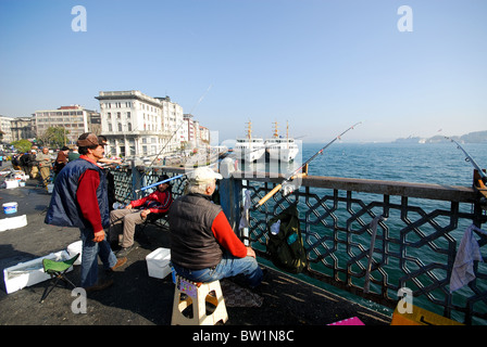 ISTANBUL, TÜRKEI. Männer Angeln von der Galata-Brücke mit dem Fährhafen in Karakoy auf der linken Seite. 2010. Stockfoto