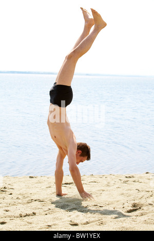 Energetische Kerl auf Arme auf Sand mit ausgestreckten Beinen stehend Stockfoto