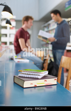 Nahaufnahme von Buch mit sieben Siegeln auf Tisch. Zwei Studenten im Hintergrund sprechen. Vertikale Form, Textfreiraum, Fokus auf Vordergrund Stockfoto