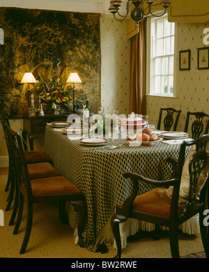 Antike Stühle am Tisch mit gemusterten Tuch im Land Speisesaal mit Tapete an der Wand über dem brennenden Lampen auf sideboard Stockfoto