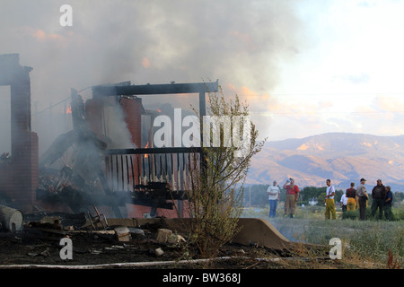 Haus in Brand und zerstörten. Mauer und Terrasse in vollen Flammen und Rauch. Totalen Verlust und Zerstörung. Feuerwehrleute beobachten. Stockfoto