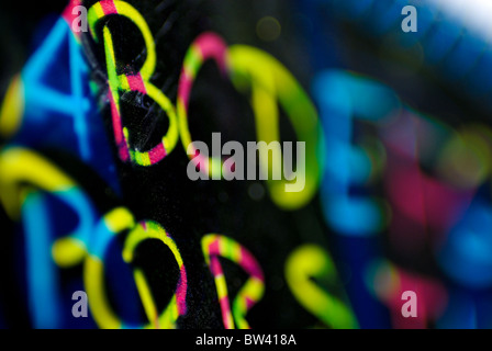 Die Buchstaben des Alphabets handschriftlich in Neon-Farben auf schwarzem Hintergrund, mit einer geringen Schärfentiefe. Stockfoto