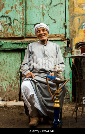 Ein freundlicher alten ägyptischen Mann sitzt an einem Straßencafé Rauchen Shisha im islamischen Kairo, Ägypten Stockfoto