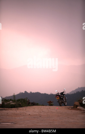 Ein Motorrad geparkt am Rand einer Klippe mit rosa Sonnenuntergang in Xishuangbanna, Südwest-China. Stockfoto