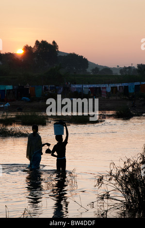 Silhouette einer indischen Frau und Junge, Waschmaschine über einen Fluss in Indien bei Sonnenaufgang. Puttaparthi, Andhra Pradesh, Indien Stockfoto