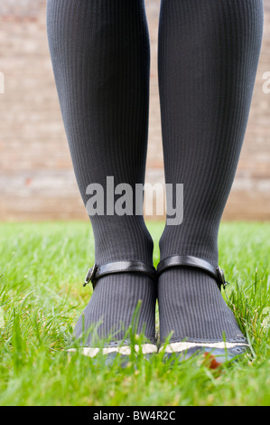 Die Füße und Beine einer Frau in grau gerippt Strümpfen tragen von Schuhen mit einem schwarzen Riemchen auf einem grünen Rasen. Stockfoto