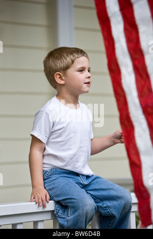 Junge sitzt auf der Veranda Geländer durch amerikanische Flagge Stockfoto