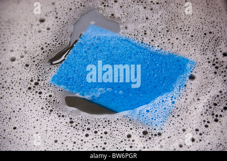 Blauer Schwamm und schmutzige Schale Wasser in ein Waschbecken Stockfoto