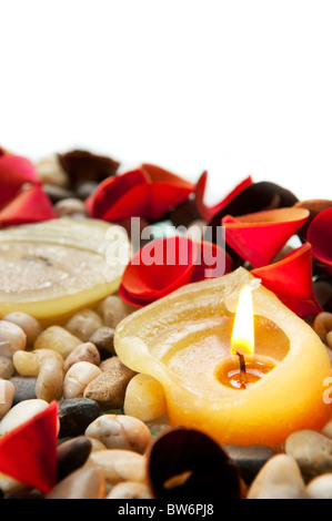 Eine brennende Kerze zwischen kleinen Steinen und hellen Blütenblätter Stockfoto