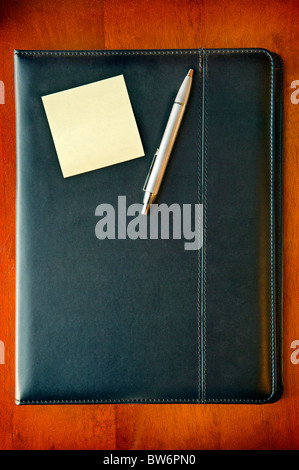 Eine schwarze executive Ordner auf Holz Schreibtisch mit Haftnotizen und Silberstift Stockfoto