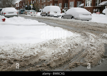 schmutzige Schnee und Reifen Spuren auf ein Gepflügtes Stadt Straßenkreuzung im Winter mit dem Auto im Schnee bedeckt Stockfoto