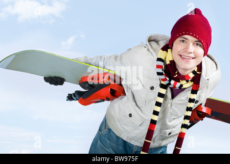 Foto von geschickten Teenager mit Snowboard hinter seinem Rücken über blauem Hintergrund Stockfoto