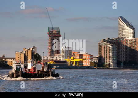 Ein Schlepper an der Themse in London Docklands, Kräne und Hochhäusern im Hintergrund Stockfoto