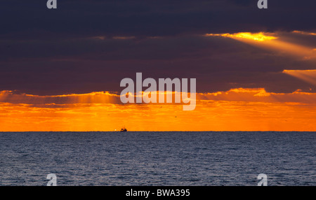 Fischerei Trawler Schiff Richtung Heimat aus dem Meer bei Sonnenuntergang, wie roll-dunkle Wolken in Brighton, England Stockfoto